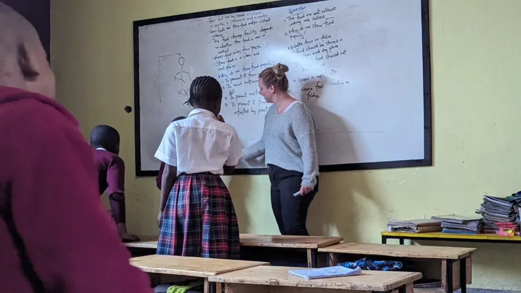 Ein Supernurse schreibt engagiert an die Wandtafel, während neugierige Schulkinder aufmerksam dem Unterricht folgen.