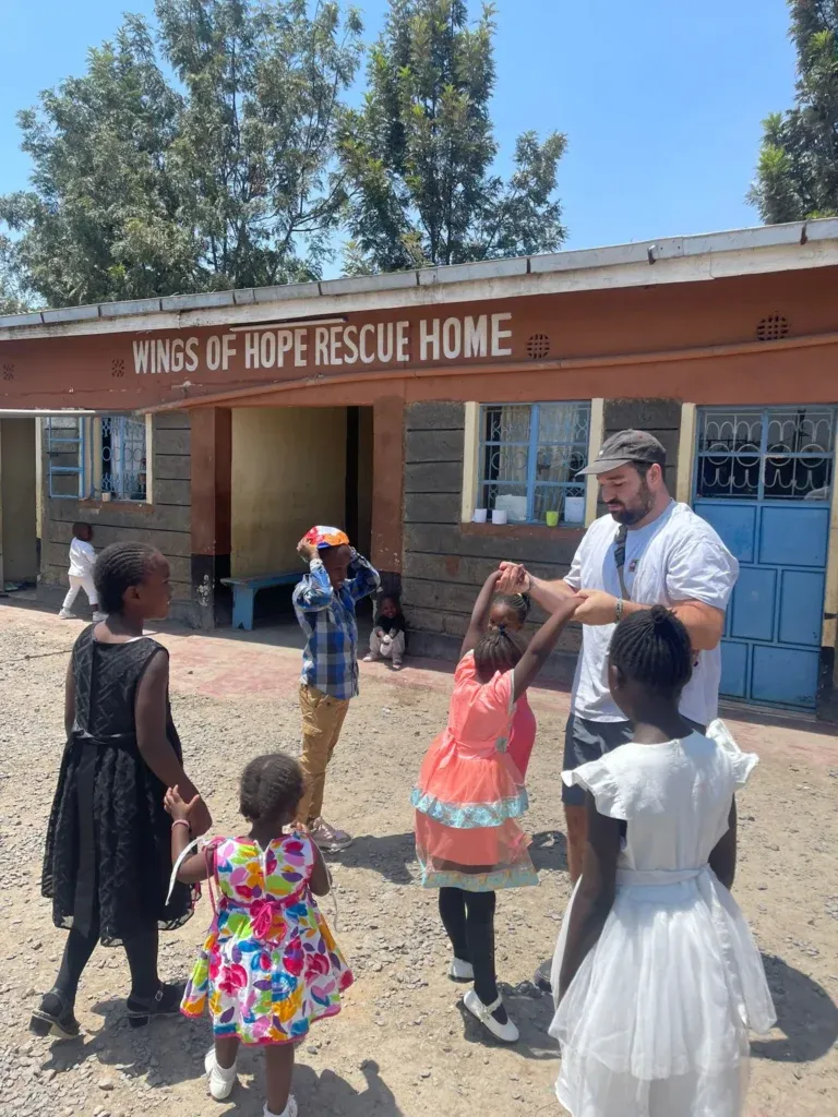 Kinder stehen fröhlich vor dem Gebäude mit der Aufschrift ‘Wings of Hope Rescue Home’, begleitet von einer Supernurse – Hoffnung und Unterstützung für eine bessere Zukunft.